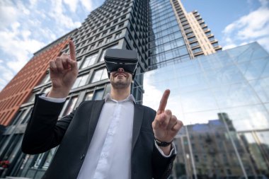 Siyah takım elbiseli, VR gözlüklü ve eğlenceli görünen bir adam.