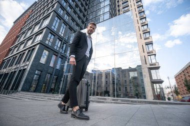 Siyah takım elbiseli genç adam bir bavul taşıyor.