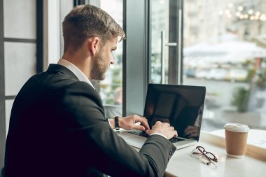 Genç işadamı bir kafede dizüstü bilgisayarda çalışıyor.