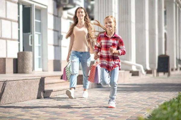 Fille souriante avec sac à provisions courant devant sa mère à l'extérieur — Photo