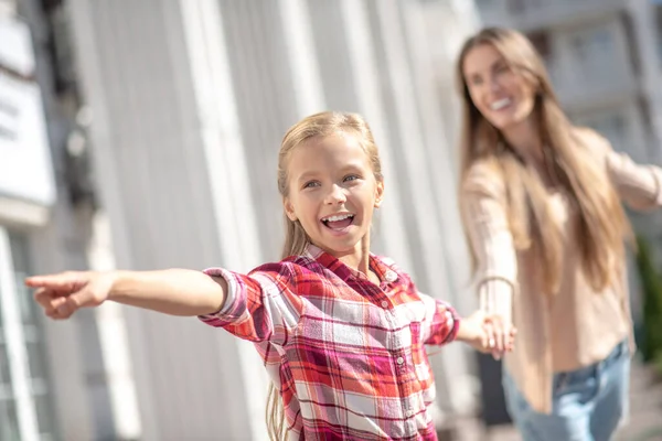 Smiling girl pointing, pulling her mom putside — Stock Photo, Image