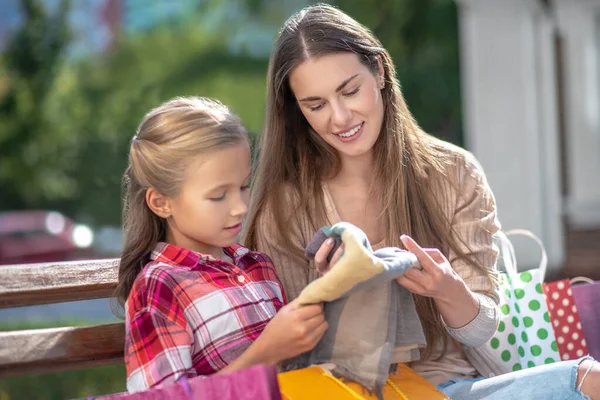 Sonriente mamá y su hija sentado en el banco del parque, admirando nueva bufanda —  Fotos de Stock