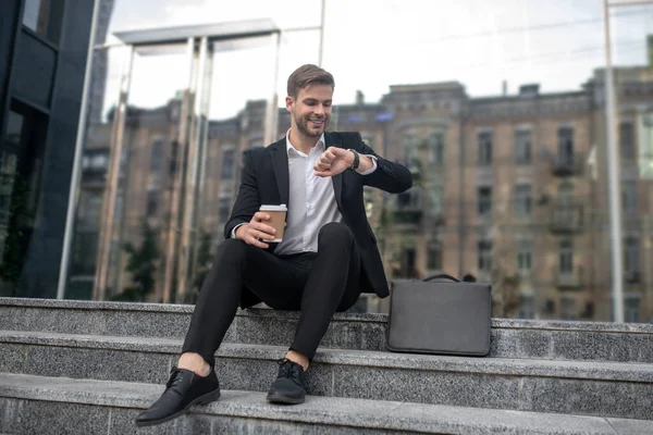 Man zakenman zittend op de trap en kijkend naar zijn horloge — Stockfoto