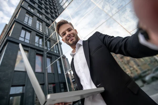 Mladý muž v černém obleku v blízkosti obchodního centra s notebookem v ruce s úsměvem — Stock fotografie