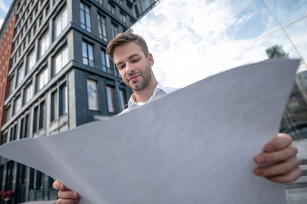 Ung man i vit skjorta håller en ritning annons ser inblandade — Stockfoto