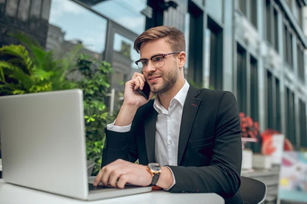 Knappe jonge zakenman met een bril aan de telefoon en glimlachend — Stockfoto