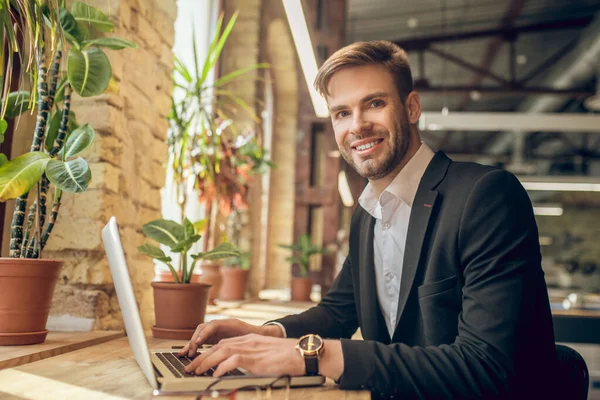 Fiatal üzletember dolgozik a laptop egy kávézóban, és mosolyogva szépen — Stock Fotó