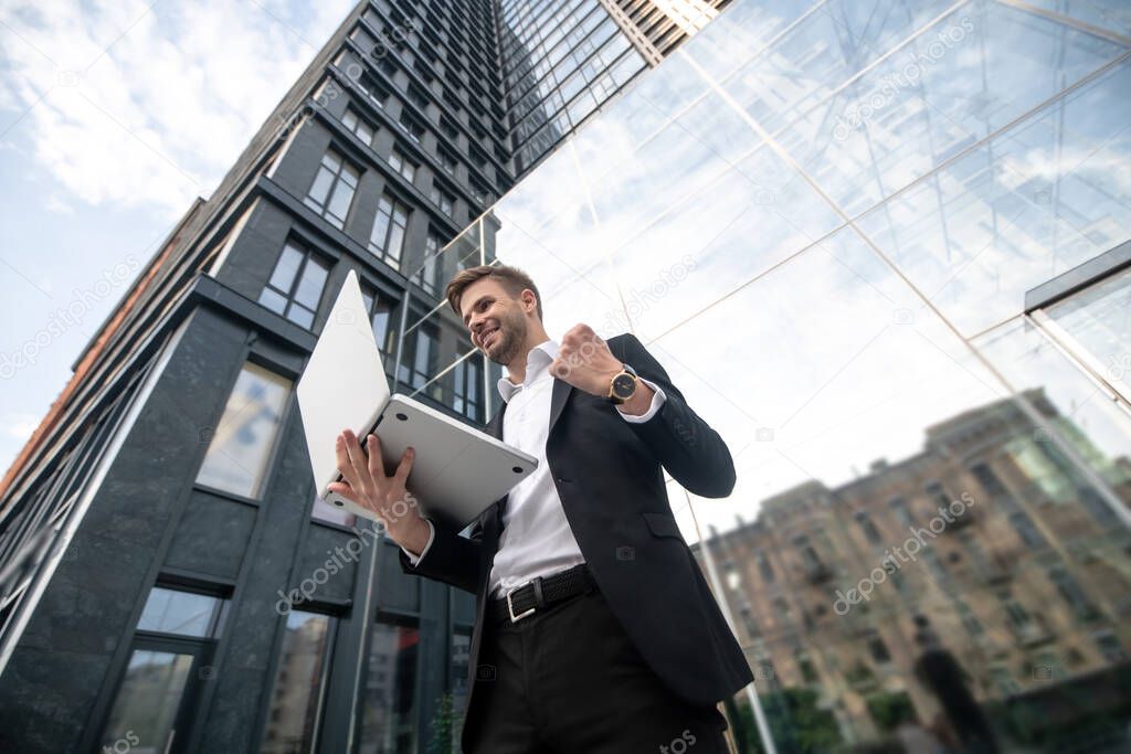 A young man in black suit near business center with a laptop in hands