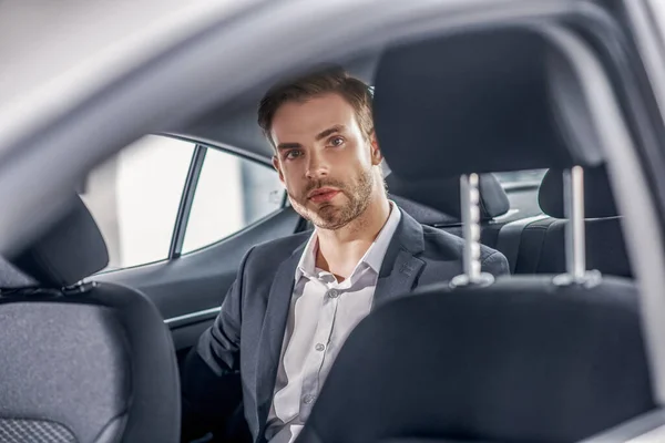 Serious brown-haired male sitting at backseat of car — Stock Photo, Image