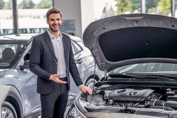 Homme aux cheveux bruns souriant pointant vers le capot ouvert de la voiture — Photo