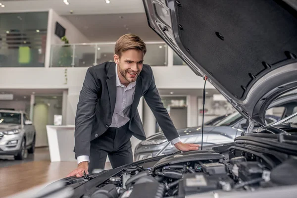 Smiling brown-haired male examining open car hood — Stock Photo, Image