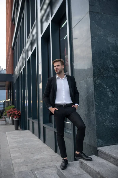 Jovem elegante em um terno preto em pé perto do edifício — Fotografia de Stock