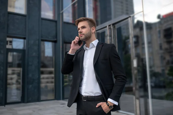 Jongeman in een zwart pak die aan de telefoon praat en er serieus uitziet — Stockfoto