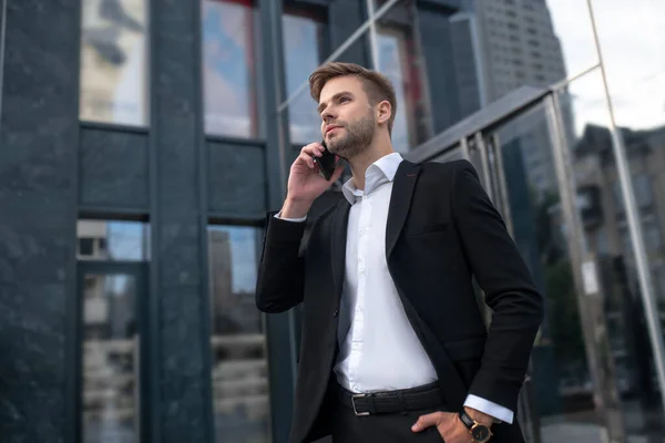 Jovem de terno preto falando ao telefone e olhando envolvido — Fotografia de Stock