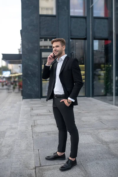 Jovem de terno preto falando no telefone perto do centro de negócios — Fotografia de Stock