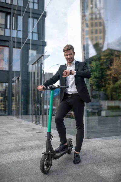 Young businessman on the scooter in the street looking at his watch — Stock Photo, Image