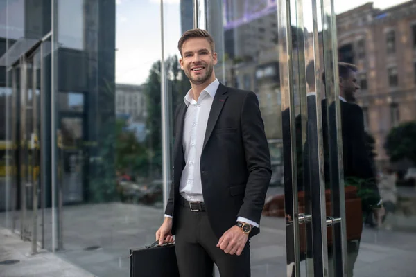 Elegante mannelijke zakenman die bij de ingang van het businesscentrum staat en glimlacht — Stockfoto