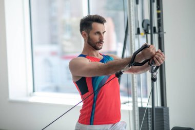 Koyu renk saçlı genç adam spor salonunda kollarıyla çalışıyor.