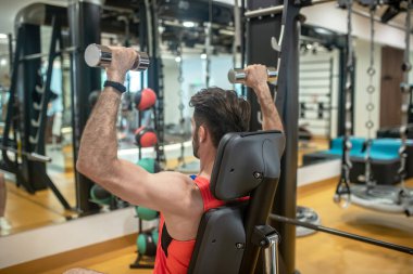 Koyu saçlı bir adam spor makinesinde kollarıyla çalışıyor.