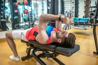 Koyu saçlı genç adam spor salonunda vücudunu geliştiriyor.