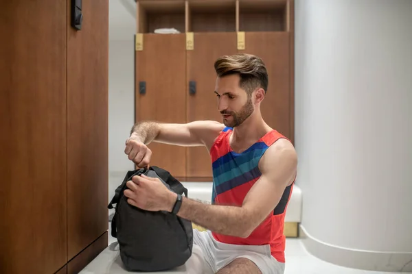 Спортивный темноволосый мужчина в яркой футболке расстегивает свою сумку — стоковое фото
