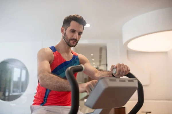 Hombre joven en camiseta brillante haciendo ejercicio en una máquina de gimnasio — Foto de Stock