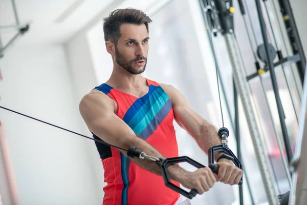 Donkerharige man werkt aan zijn armen in de sportschool en ziet er geconcentreerd uit — Stockfoto