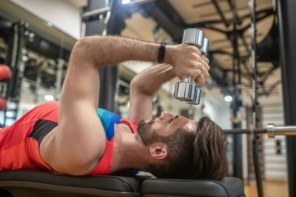 Joven hombre moreno en camiseta brillante trabajando en su cuerpo en el gimnasio — Foto de Stock