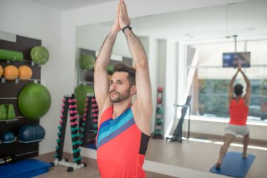 Sakallı erkek yoga yapıyor, savaşçı pozisyonunda duruyor.