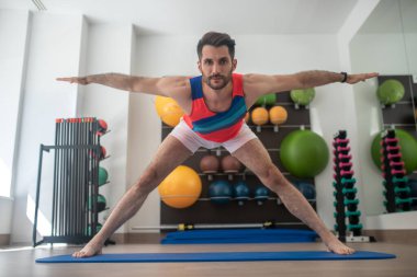 Sakallı erkek, geniş bacaklı, elleri açık duruyor.