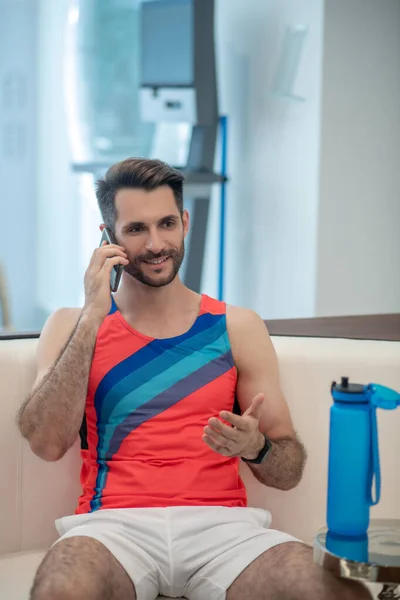 Бородатый мужчина в спортивной одежде разговаривает по телефону в спортзале — стоковое фото