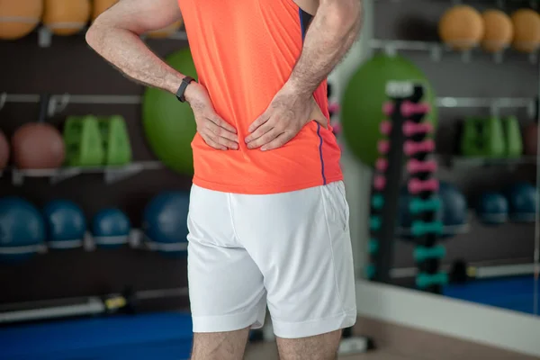 Närbild av manliga händer röra smärtsam rygg i gymmet — Stockfoto