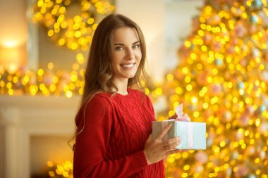 Koyu saçlı genç bir kadın elinde bir Noel hediyesi tutuyor.