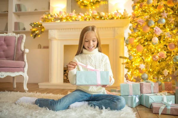 Blond söt flicka ser glad ut samtidigt som hon håller i sin presentförpackning — Stockfoto