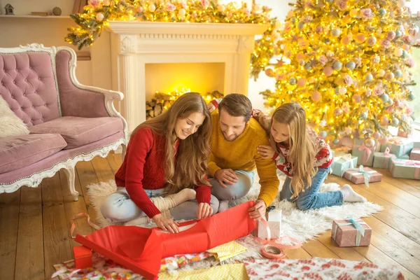 Junge Familie sitzt auf dem Boden und packt Neujahrsgeschenke ein — Stockfoto