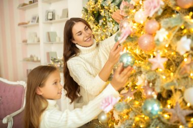 Anne ve kızı birlikte Noel ağacı süslüyorlar ve mutlu görünüyorlar.