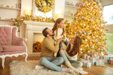 Genç aile yeni yıl ağacının yanında oturmaktan mutlu.