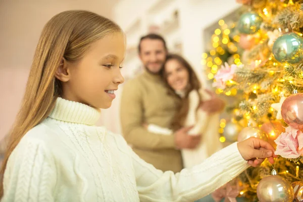 Papá poniendo pelotas en el árbol de navidad mientras su esposa e hija lo miran — Foto de Stock