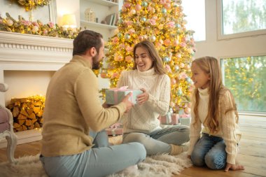 Genç bir aile yerde oturup Noel hediyelerini değiş tokuş ediyor.