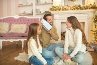 Genç bir aile yerde oturuyor ve Noel hediyeleri için heyecanlanıyor.