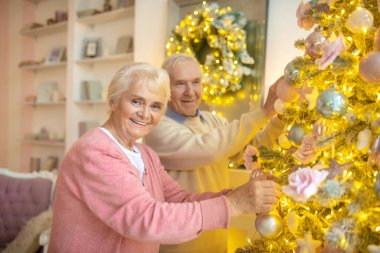Yaşlı çift Noel ağacını süslüyorlar ve kendilerini iyi hissediyorlar.