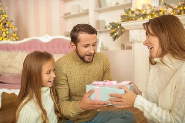 Jonge familie zit op de vloer en wisselt kerstcadeaus uit — Stockfoto