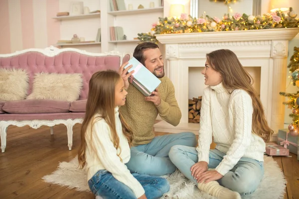 Ung familj sitter på golvet och vimlar av glada över julklappar — Stockfoto
