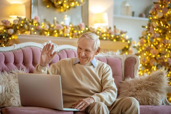 Siwe włosy starzec siedzi na kanapie i ma wideo rozmowy — Zdjęcie stockowe