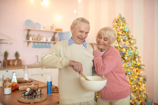 Pareja mayor de pie en la cocina, hombre revolviendo algo en un tazón — Foto de Stock