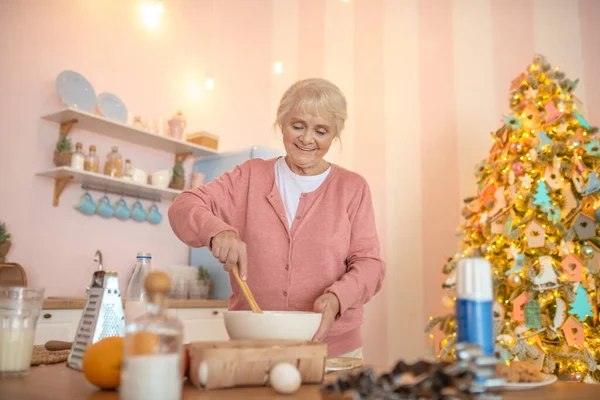 Улыбающаяся седовласая женщина готовит что-то на кухне — стоковое фото