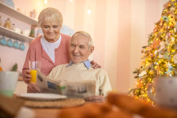 Grauhaariger Mann sitzt am Tisch, während seine Frau ihm Orangensaft gibt — Stockfoto