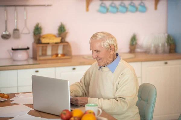 Старший человек сидит за столом и работает над ноутбуком — стоковое фото