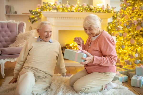 Idős nő nyitó karácsonyi ajándék a férjétől, és boldognak néz ki — Stock Fotó