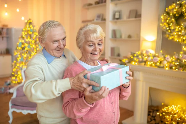 Starszy mężczyzna daje prezent świąteczny żonie i uśmiecha się — Zdjęcie stockowe